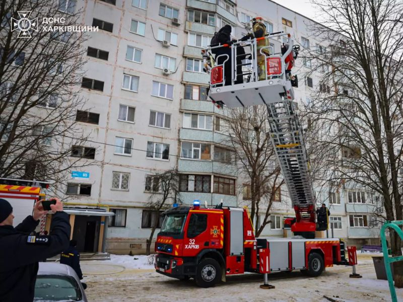 Рятувальники ДСНС на пожежній автодрабині Volvo здійснюють рятувальні роботи у багатоповерхівці Харкова. Червона спецтехніка 32-ї частини розгорнута біля житлового будинку взимку.