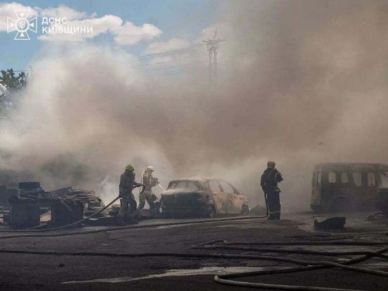 Співробітники ДСНС гасять згорілі автомобілі на відкритому майданчику в умовах сильного задимлення.