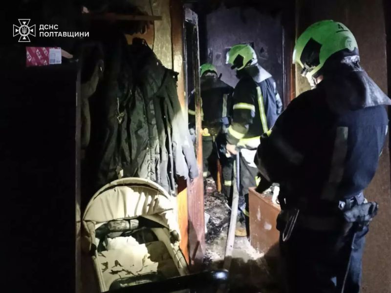 Рятувальники ДСНС Полтавщини ліквідовують пожежу в житловому будинку. У задимленому коридорі біля дитячого візочка працюють вогнеборці в захисному спорядженні з ліхтарями.
