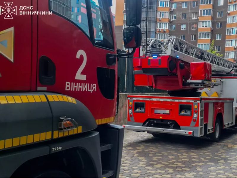 Пожежна автоцистерна та автодрабина ДСНС біля багатоповерхового житлового будинку у Вінниці під час евакуації людей та гасіння пожежі на верхніх поверхах.