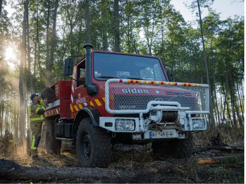 Пожежний автомобіль ДСНС та рятувальник із пожежним рукавом на місці ліквідації загоряння в лісі зони відчуження.