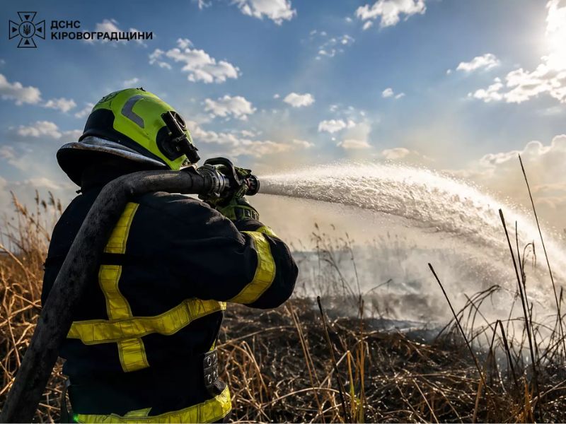 Рятувальник ДСНС ліквідовує загоряння сухостою за допомогою пожежного рукава поблизу Кропивницького.