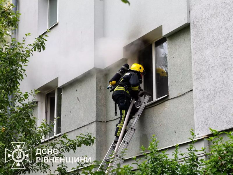 Рятувальник ДСНС Рівненщини ліквідовує пожежу на другому поверсі будівлі, подаючи воду з ручного пожежного ствола через вікно.